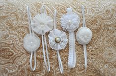 three white hair clips with flowers and pearls on them sitting on a lace covered surface