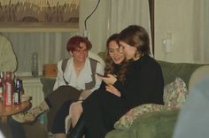 two women sitting on a couch looking at their cell phones while another woman stands in the background