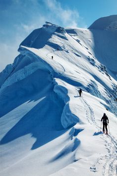 two people hiking up the side of a snow covered mountain