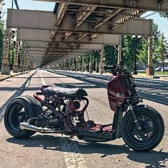 the motorcycle is parked on the side of the road under an overpass with trees in the background