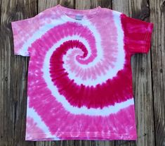 a pink and white t - shirt with a spiral design on the front, against a wooden background