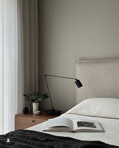 an open book sitting on top of a white bed next to a lamp and window