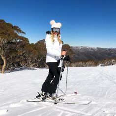 a woman standing on top of a snow covered slope wearing skis and holding ski poles