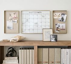 a shelf with books and pictures on it next to a wall mounted calendar, framed photos, and other items