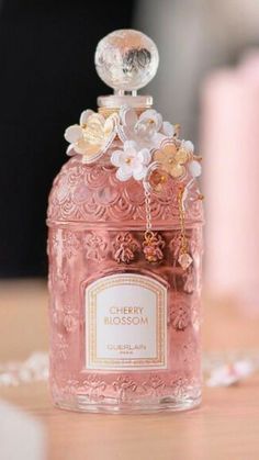 a pink bottle with flowers on it sitting on top of a wooden table next to a chain