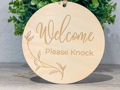 a wooden sign that says welcome please knock on the side of a table next to a potted plant