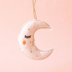 Photo is a felted moon ornament hanging on a jute piece of string.  The moon is white with black eyelashes and an orange circle cheek.  The moon also has silver sequins sewn onto it. Handmade Star Ornaments, Sun Felt Ornament, Felt Moon Ornaments, Moon Felt Ornament, Felt Moon, Moon Christmas, Moon Ornament, Felted Wool Crafts, Sweets Gift