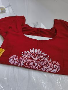 a red shirt with white designs on it sitting on top of a plastic wrapper