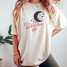 Get ready to be OBSESSED with your new Its a Wonderful Life shirt. It's the cutest and most trendy way to combine all those important trendy vintage and retro christmas vibes! This is the perfect holiday shirt!  * Q U I C K * F A C T S * ✺  All shirts are UNISEX ✺  100%  ringspun cotton (fiber content may vary for different colors) ✺  Soft-washed, garment-dyed fabric brings extra coziness ✺  Wash and dry normally (on cool for best results) ✺  Sewn-in twill label * S I Z I N G * ✺ For an oversized fit, select two or three sizes up from your normal size ✺ Model is wearing size L  ✺ Sizing runs true to size ✺ Relaxed fit ✺ Most women find their typical size works best, since they are meant to fit a touch loose ✺ See Size guide and fit in images          * S H I P P I N G * T I M E S * ✺ Our i Holiday Cotton Graphic Tee Shirt, Cotton Graphic Tee Shirt For Holidays, Casual Cotton Tops For Holiday, Cute Cotton Holiday Tops, Holiday Cotton Tops With Letter Print, Trendy Cotton Christmas Tops, Holiday Cotton Shirt With Crew Neck, Crew Neck Cotton Shirt For Holiday, Bedford Falls