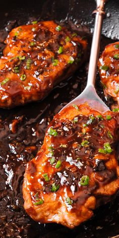 two pieces of meat covered in sauce and green onions on a skillet with a spatula