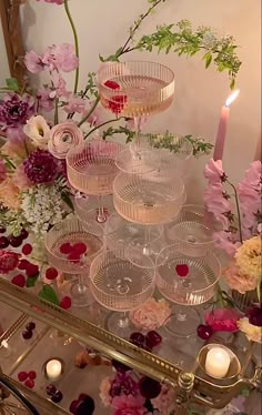 there are many glasses on the table with flowers and candles around it, as well