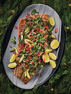 an overhead view of a pizza on a platter with greens, onions and limes