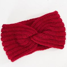 a red knitted headband with a knot on the top and bottom, sitting on a white surface