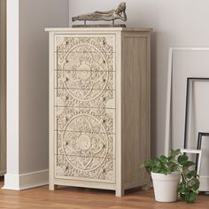 a white cabinet sitting on top of a wooden floor next to a potted plant