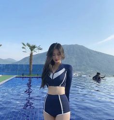 a woman standing in front of a swimming pool wearing a blue and white swim suit