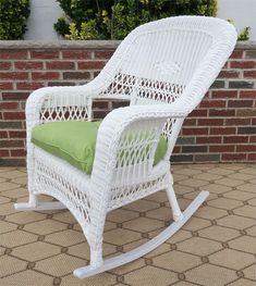 a white wicker rocking chair with green cushion on a patio floor next to a brick wall