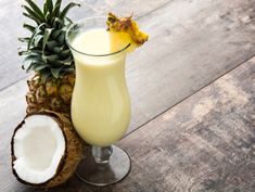 a pineapple drink in a tall glass next to a cut up coconut