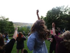 a group of people standing on top of a lush green field holding their hands in the air