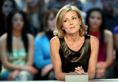 a woman sitting at a table in front of a group of people with her hands folded