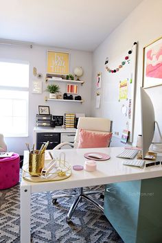 a white desk topped with a laptop computer next to a pink and blue ottoman covered in pillows