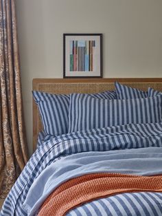 a bed with blue and white striped comforter next to an orange throw pillow on top of it