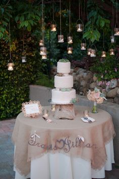 a table topped with a white cake covered in frosting and surrounded by hanging lights