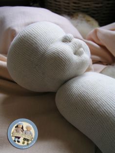 a white stuffed animal laying on top of a bed next to a pink blanket and a button