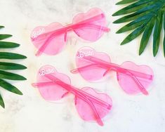 three pink heart shaped sunglasses with the word barbie written on them and palm leaves in the background