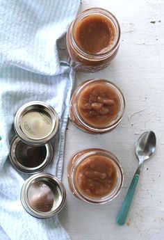 four jars with peanut butter and spoons next to each other on a white surface