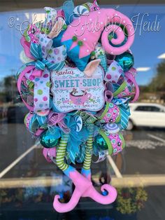 a pink and blue wreath is hanging in front of a store window with the words sweet shop on it