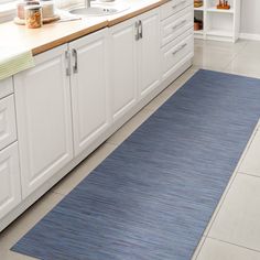 a kitchen with white cabinets and blue rugs on the floor in front of sink