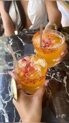 two people holding up glasses with drinks in them on top of a marble countertop