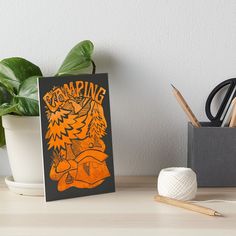 an orange and black poster with the words camping on it art boarder next to a potted plant