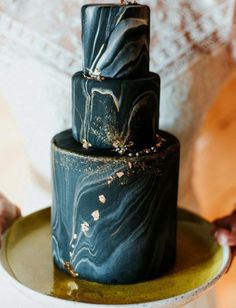 a woman holding a plate with a black cake on it's side and gold decoration