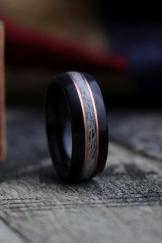 a black and rose gold wedding ring on top of a wooden table