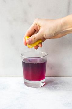 a hand holding a piece of food over a glass filled with purple liquid on top of a white counter