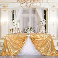 the table is covered with gold sequins and white flowers in front of a chandelier