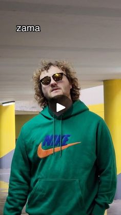 a man in a green hoodie and sunglasses standing next to a yellow pillar with the word nike on it