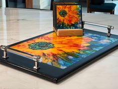 a painting is sitting on top of a glass tray with a wooden stand in front of it