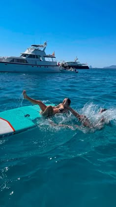 a man laying on a surfboard in the ocean next to a boat and yacht