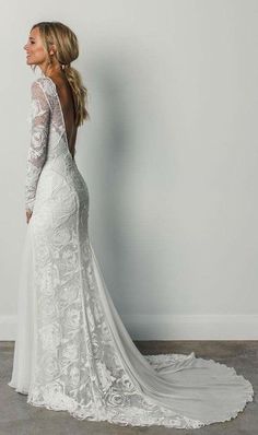 a woman in a white wedding dress standing against a wall with her back to the camera