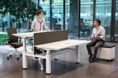 two people sitting at desks in an office setting, one talking to the other