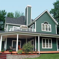 a large green house with white trim on the front porch and second story balcony area