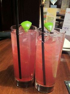 two glasses filled with red liquid and green garnish on top of a wooden table