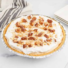 a pie topped with whipped cream and pecans on a white countertop next to a striped napkin