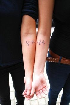 two people holding hands with tattoos on their arms and the word love written in cursive writing