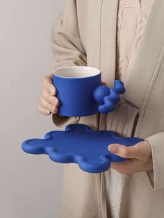 a woman holding a blue coffee cup in one hand and a mug in the other