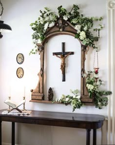 a cross hanging on the wall next to a table with flowers and candles in front of it