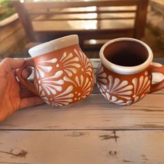 two coffee mugs sitting on top of a wooden table next to eachother