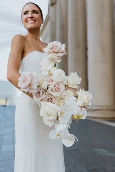 a woman in a white dress holding a bouquet of flowers and smiling at the camera